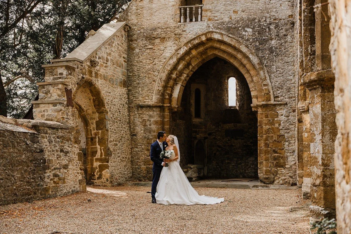 Wedding couple kissing inside historic stone ruins surrounded by old stone walls and arches.