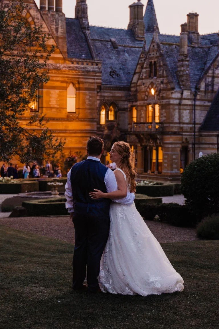 A bride and groom dance outside a castle-like building at sunset