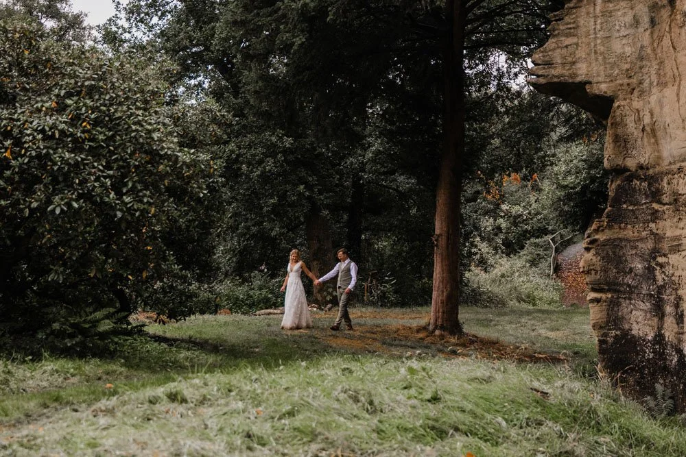 A bride and groom walking by the cliffs and trees at Guys Cliffe House
