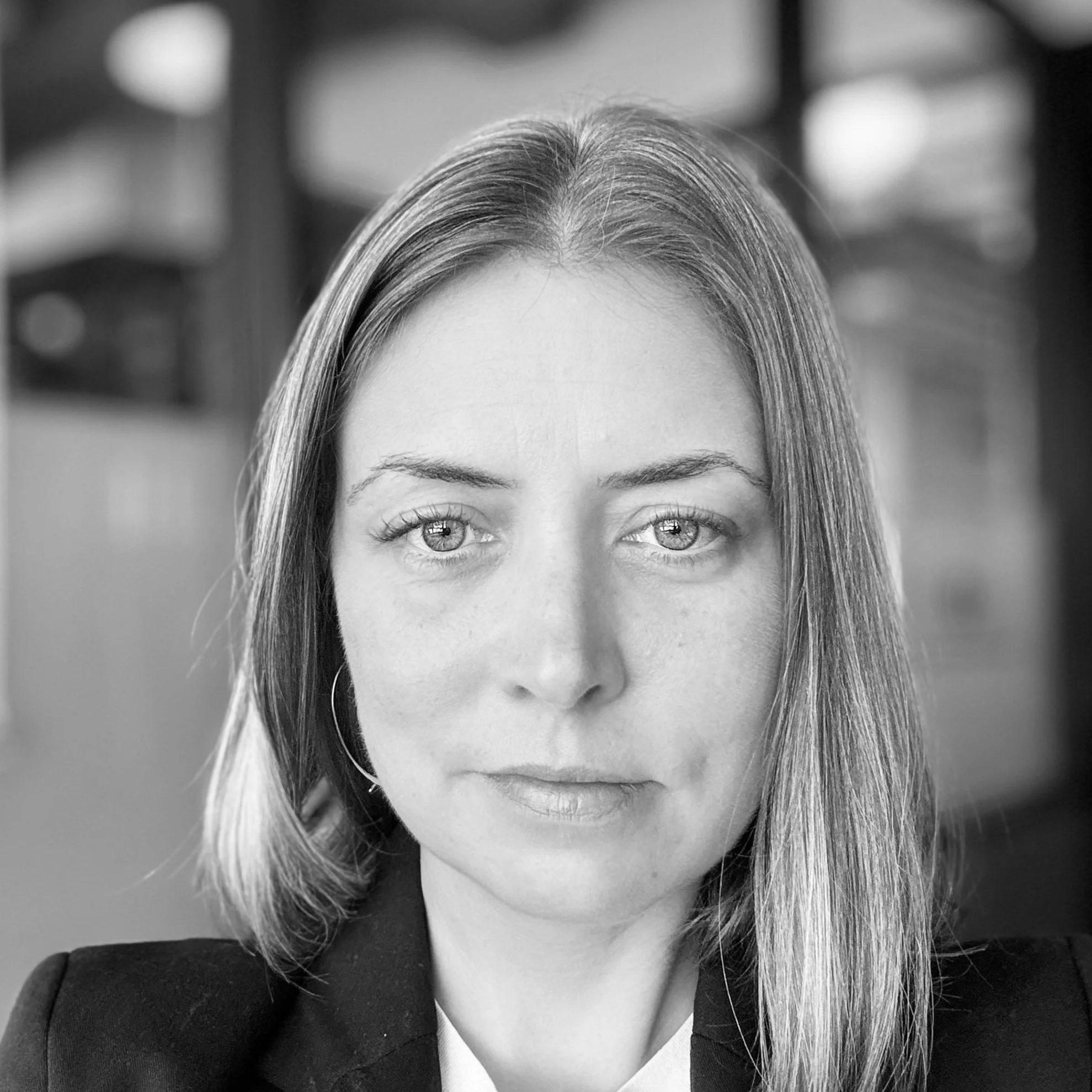 Black and white portrait of a woman with shoulder-length hair, wearing a blazer, with a blurred background.