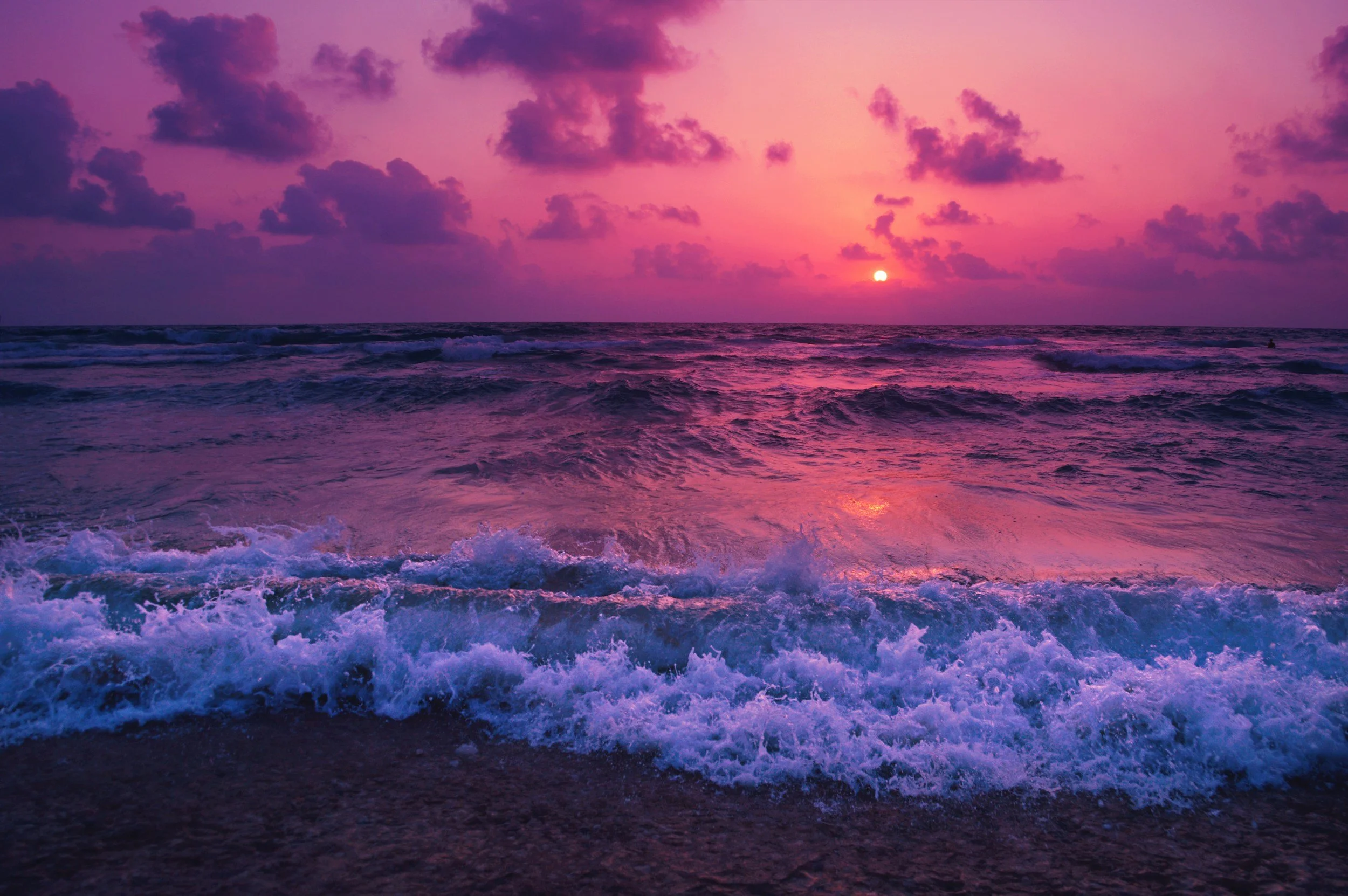 Vibrant purple and pink ocean sunset with waves and clouds.