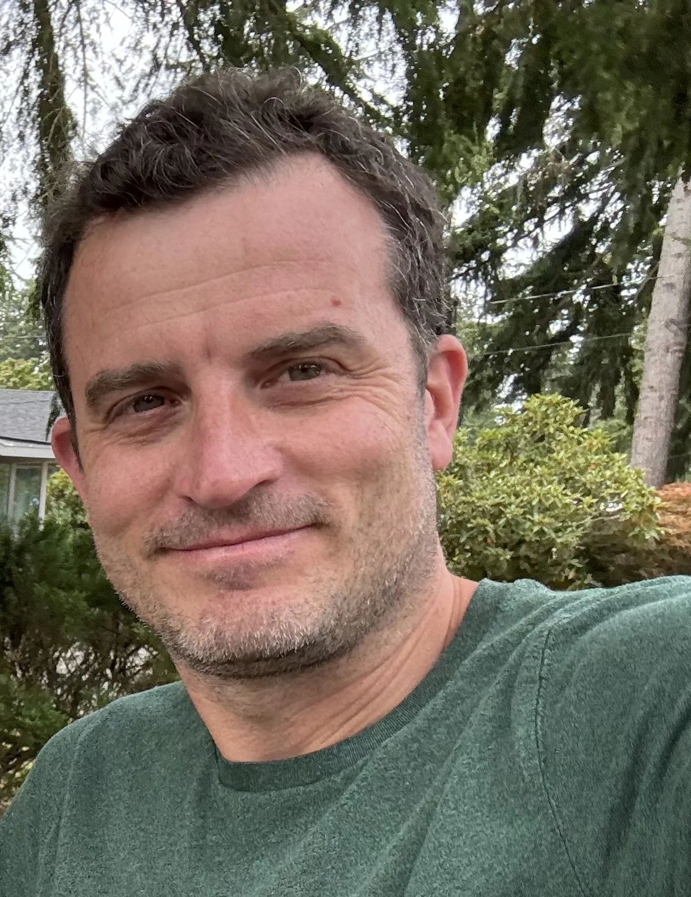 A woman smiling while sitting on a brown leather couch in a cozy indoor setting.