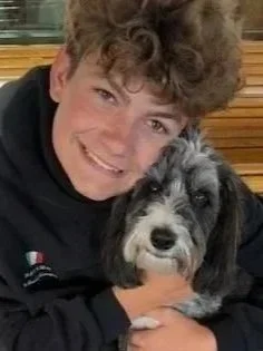 Smiling young man with curly hair holding a small black and white dog.