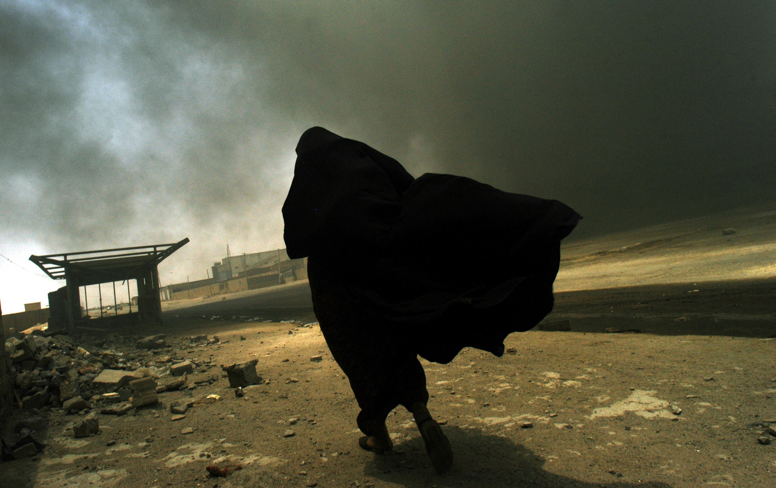  An Iraqi woman walks through a plume of smoke rising from a massive fire at a liquid gas factory as she searches for her husband in the vicinity of the fire in Basra, Iraq, May 26, 2003.  The fire was allegedly started by looters picking through the