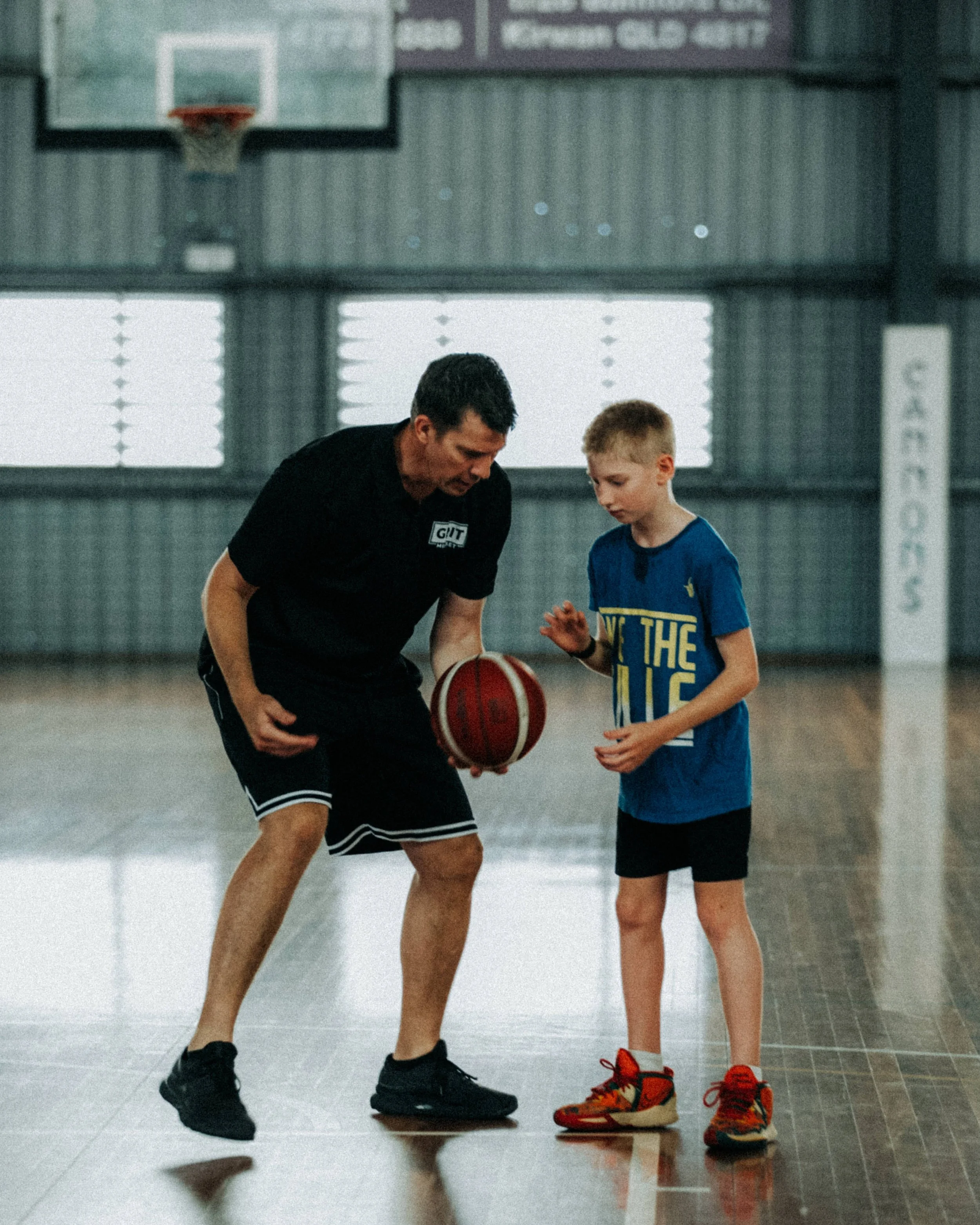 A coach teaching a young boy how to play basketball inside a gymnasium.
