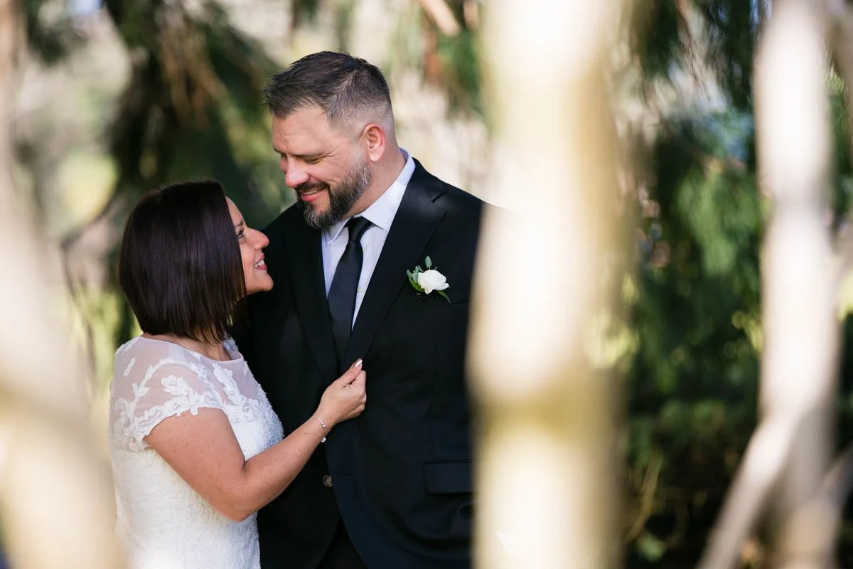 A bride and groom sharing an intimate moment outdoors, framed by trees, during their wedding.
