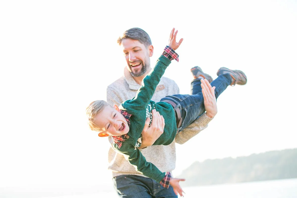 A man lifting a young boy in the air outdoors during daytime, both smiling and happy.