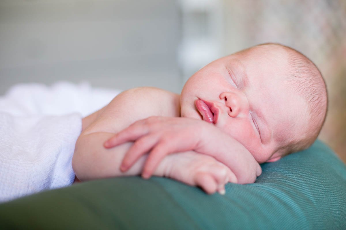 Sleeping newborn baby with closed eyes, resting on a person's arm.