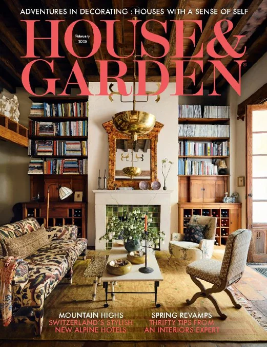 Cover of House & Garden magazine featuring a cozy living room with a white fireplace, surrounded by built-in bookshelves filled with books, a patterned sofa, an armchair, and decorative accents, with the magazine's title in large pink letters at the top.