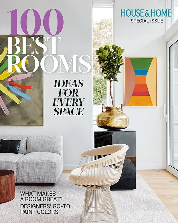 Cover of a home decor magazine featuring a modern living room with artwork, a beige armchair, a corner table, a gray sofa with pillows, a potted plant, a large abstract painting, and text about the best rooms and design ideas.