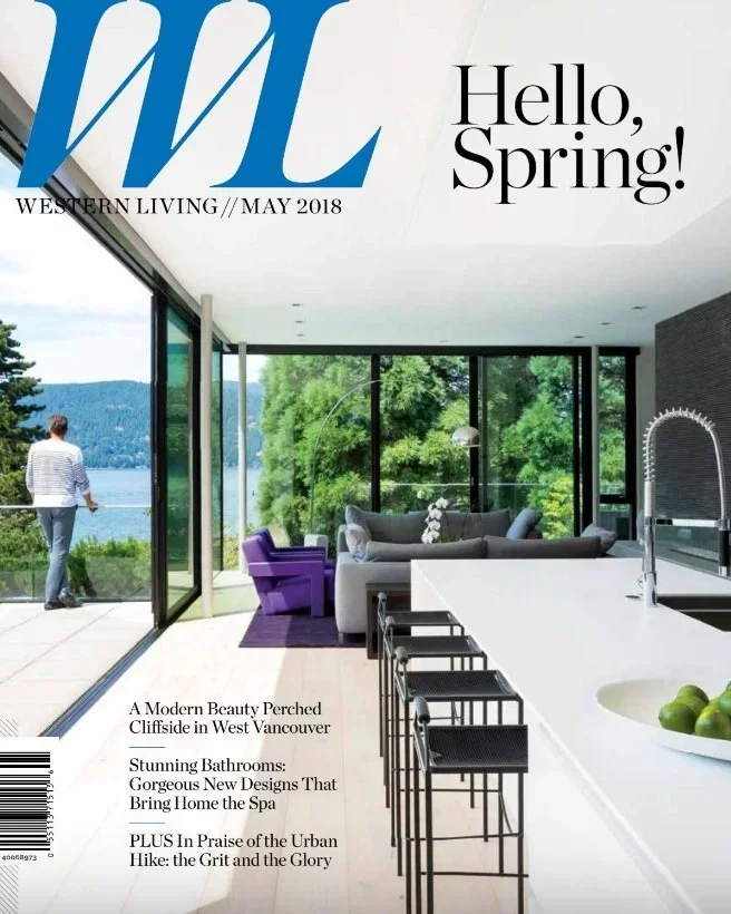 Cover of Western Living magazine, May 2018 issue, featuring a modern interior with large glass windows overlooking lush greenery and a lake, with indoor furniture including a sofa, purple chair, and bar stools.