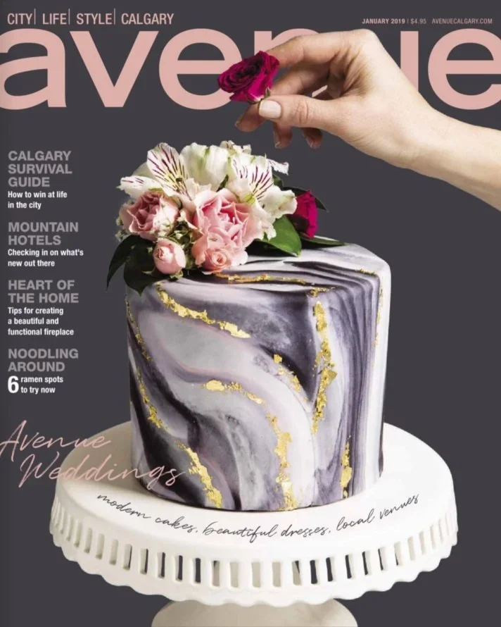 Magazine cover featuring a marble-patterned wedding cake with flowers on top, a hand placing a flower, and text about Calgary wedding guides and venues.