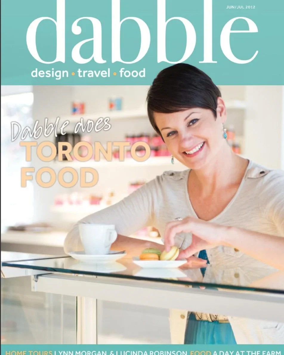 Cover of Dabble magazine, June/July 2012 issue, featuring a smiling woman with short dark hair, wearing a light-colored top, sitting at a counter with a white cup and colorful macarons, in a bright, modern kitchen setting.