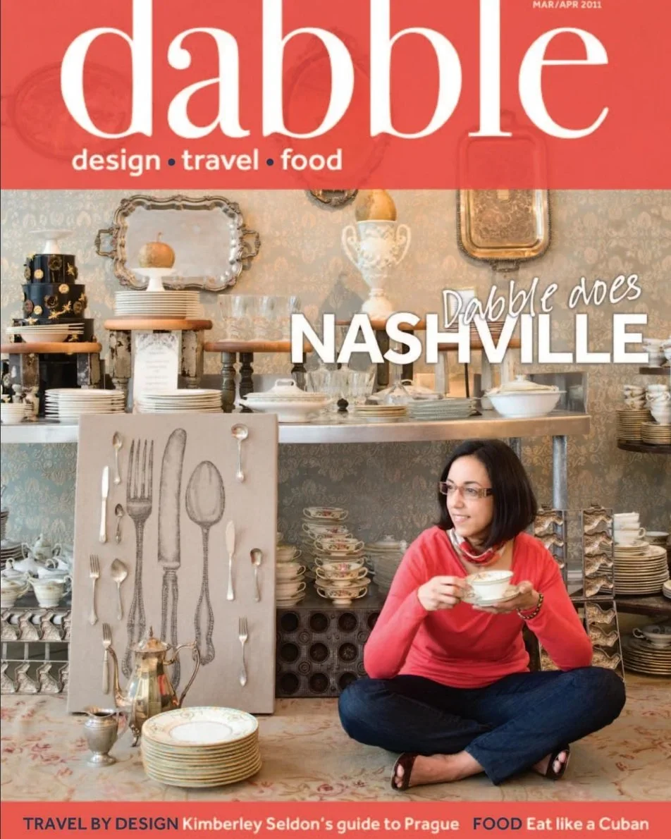 Cover of Dabble magazine, March/April 2011 issue, featuring a woman sitting cross-legged, drinking from a bowl in front of a display of plates, bowls, and decorative dishes in a vintage-style setting.