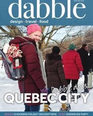 People walking outdoors in winter, some wearing colorful winter jackets and hats, with snow on the ground and leafless trees in the background.