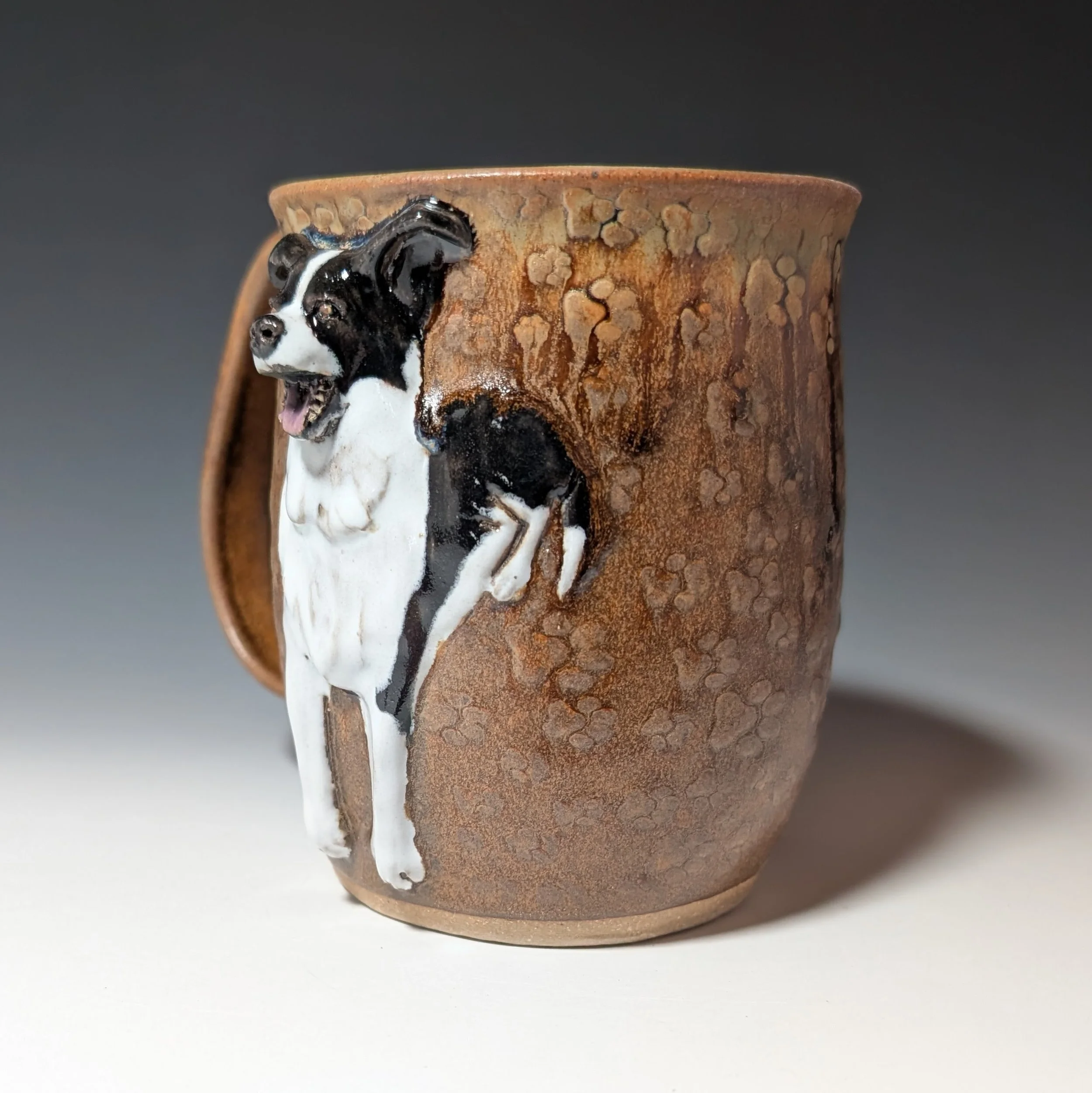Black and white dog relief on a brown handmade ceramic mug.