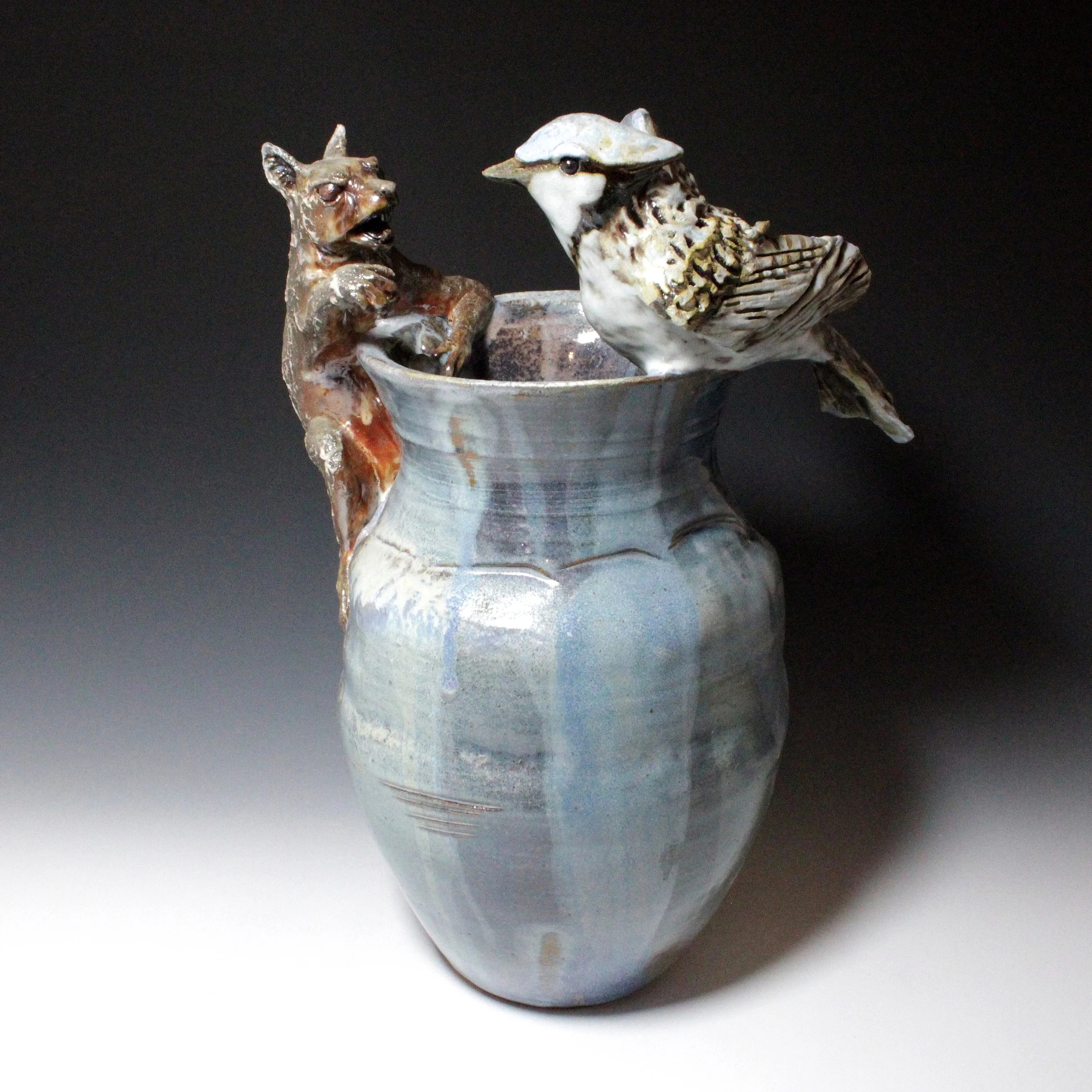 Quite a fight is playing out on this large blue vase textured on the shoulder. A Blue Jay hopes to capture a frog from an enraged squirrel; two foes in a battle over food.
