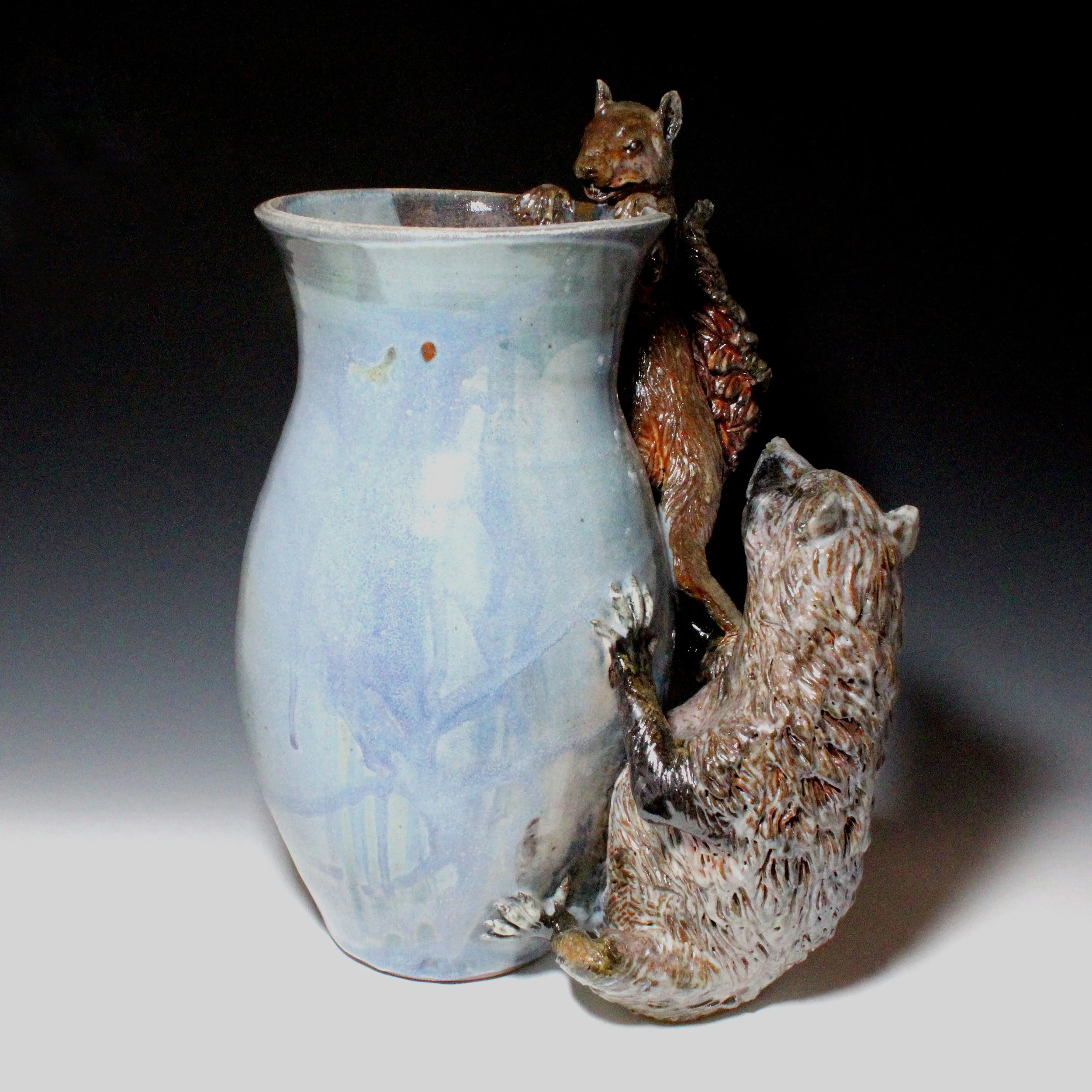 The red color  on the squirrels belly, tail and face is created by starving the fire of oxygen in the kiln forcing it to pull oxygen out of the glazes in the pot leaving a red color behind.