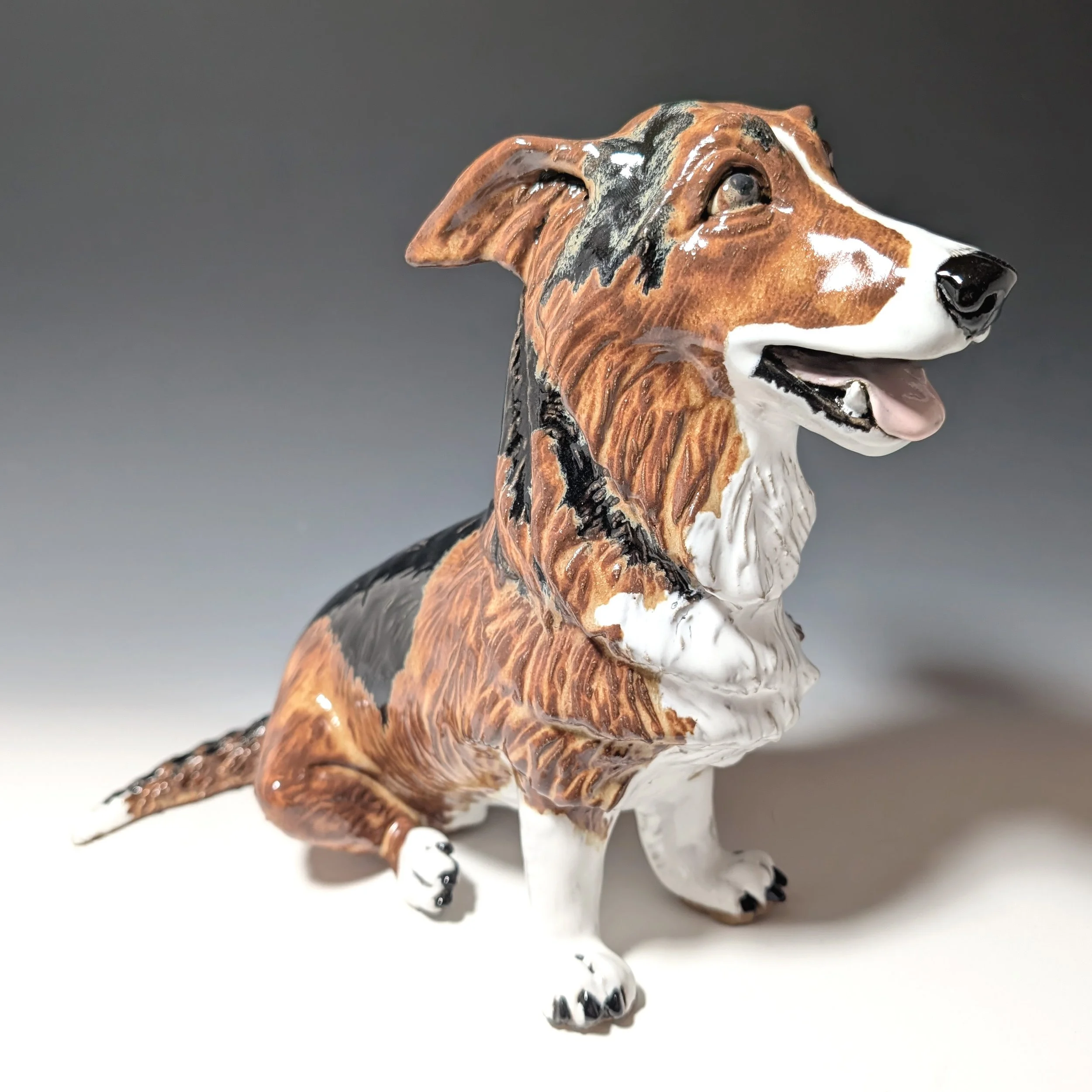 Clay sculpture of a tri-color corgi dog smiling with tongue out.