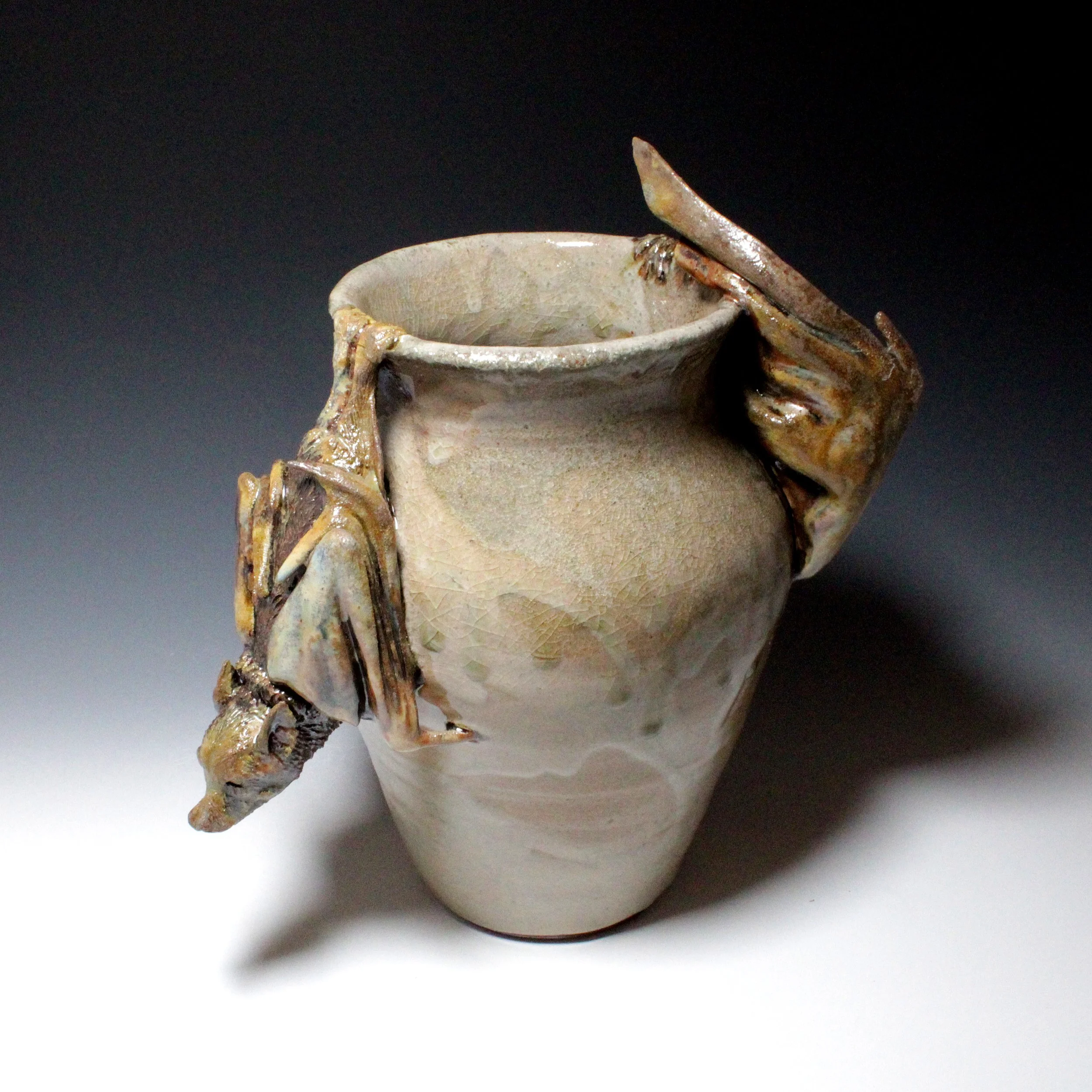 Two Asian flying foxes hang on this smooth tan vase resting.