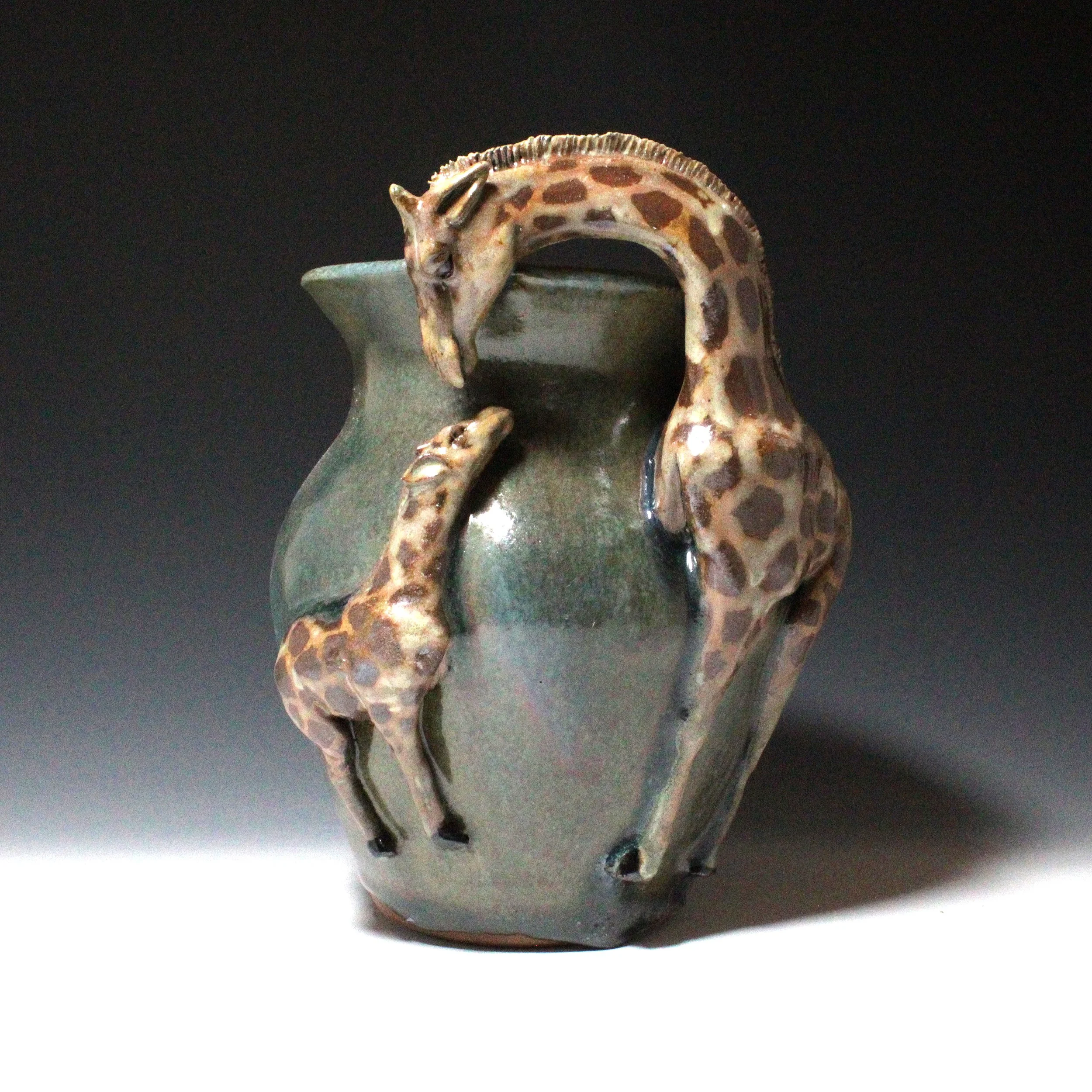 A giraffe mother shows love to its child with head down ready to lick the baby giraffes head on this green and blue vase. 