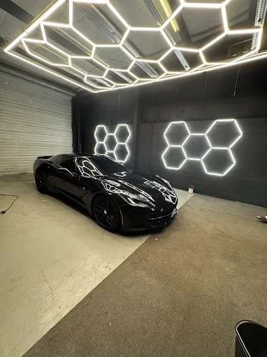 Black sports car in a modern garage with hexagonal neon light decorations on the wall and ceiling.