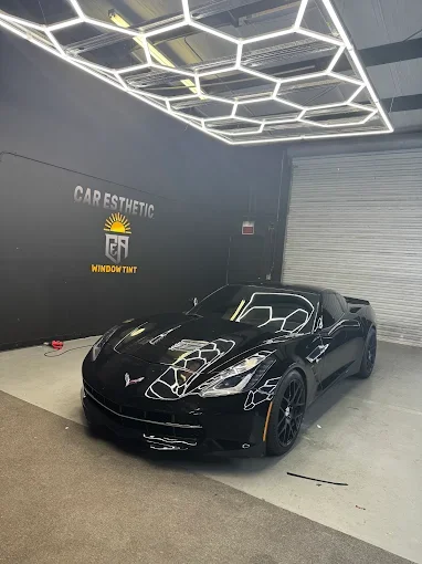 Black Chevrolet Corvette sports car inside a showroom with geometric LED ceiling lights and a gray wall that reads "CAR AESTHETIC" and "WINDOW TINT".