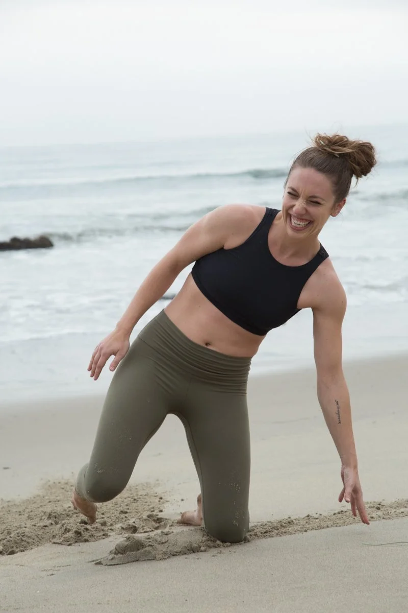 Girl wearing yoga clothes laughing while kneeling on beach in Malibu, California