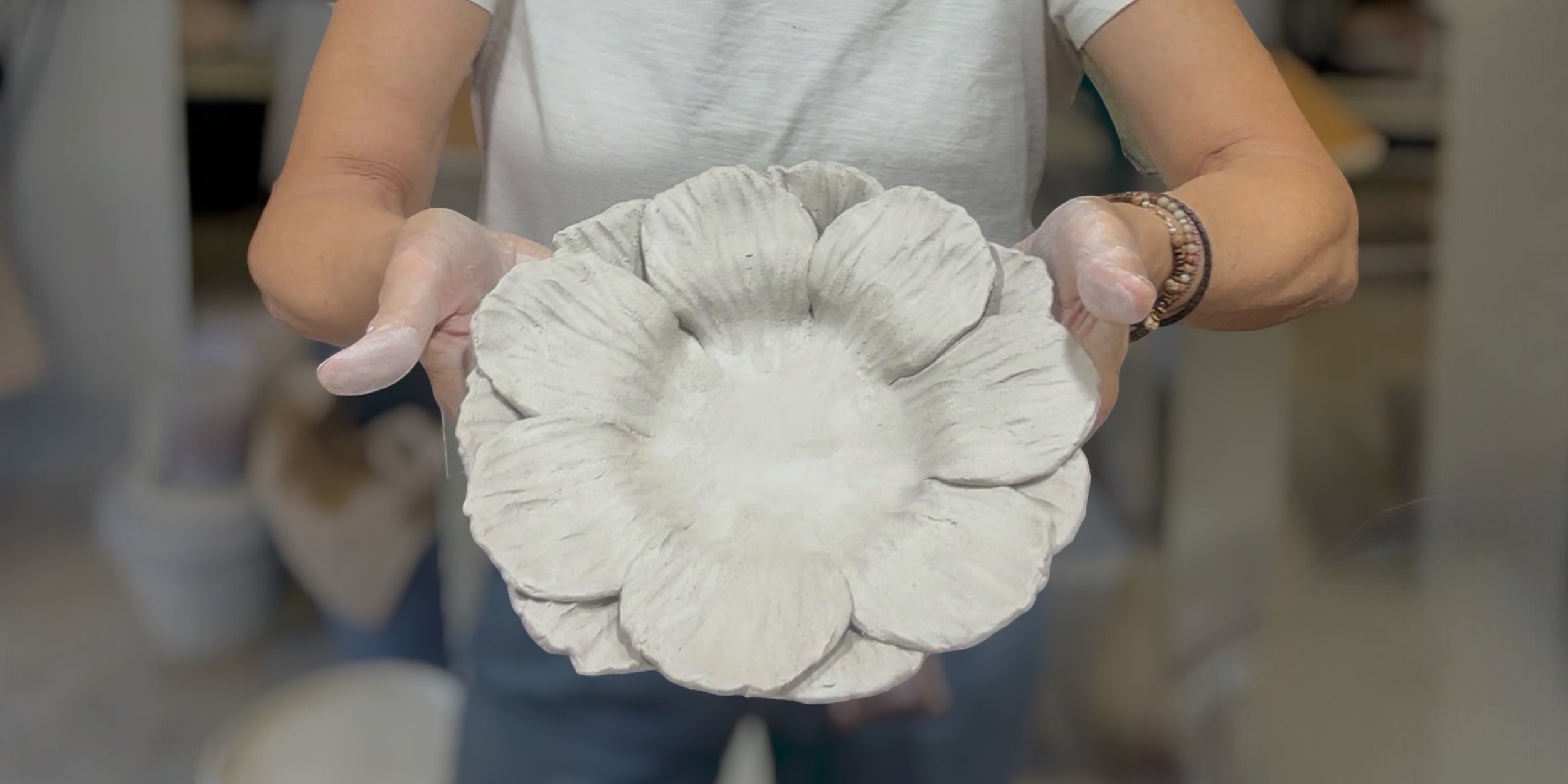 a petal bowl being held by hands covered in clay