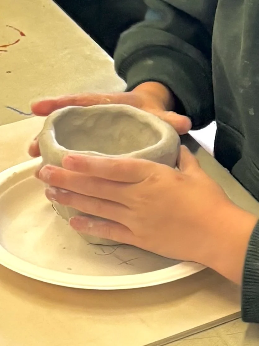A student holding a handmade pottery cup during a primary school pottery class