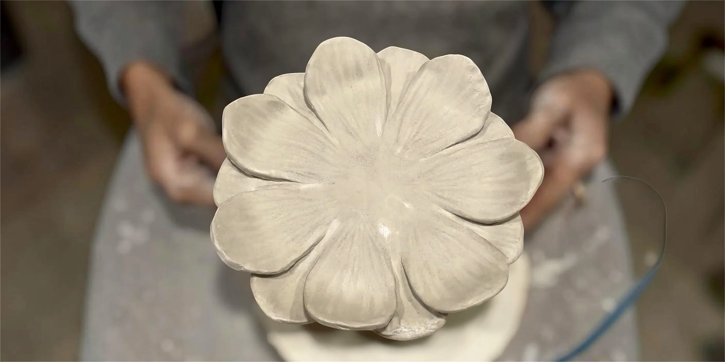 a petal bowl being held by hands covered in clay