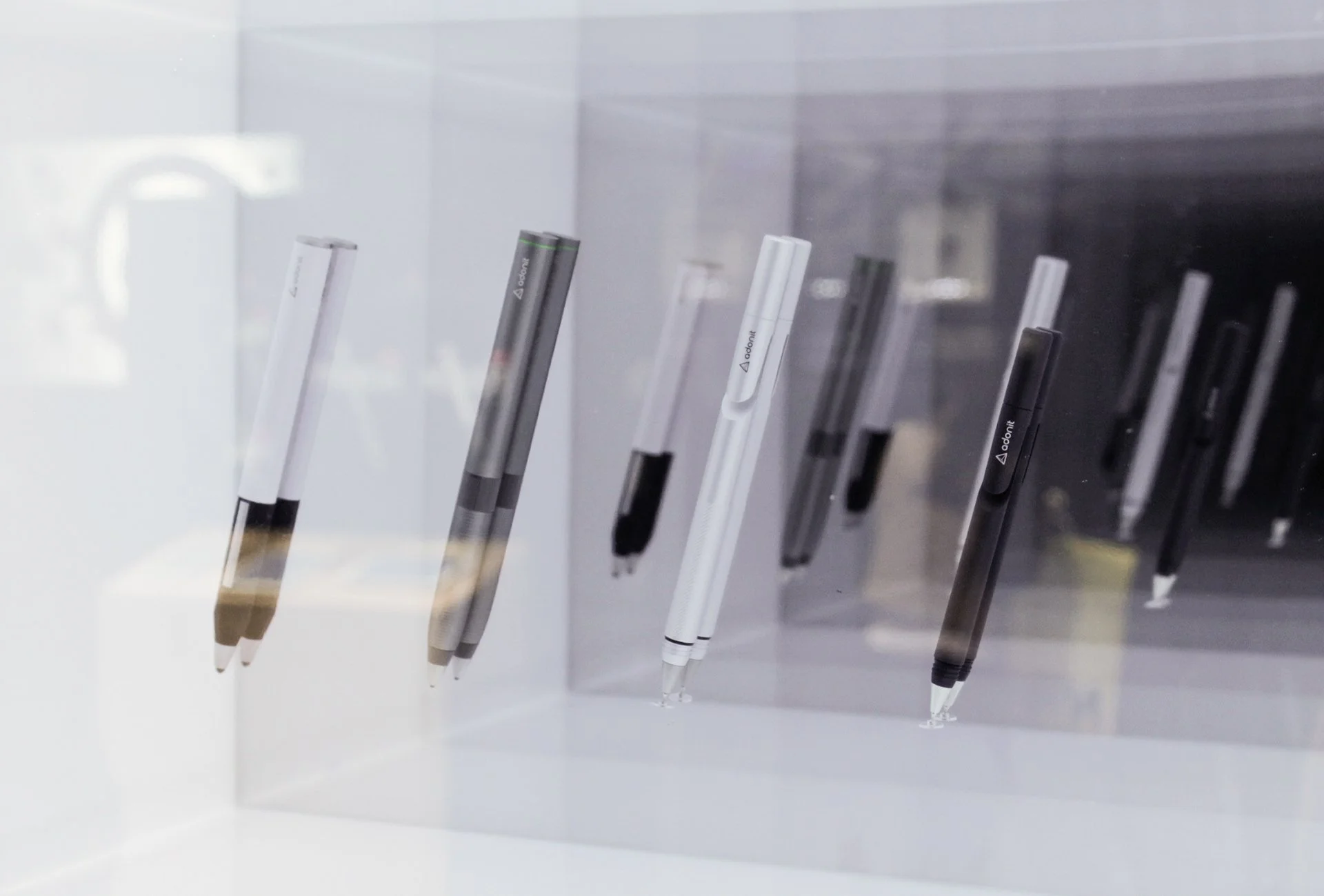 Several Adonit electronic stylus pens displayed vertically in a row behind a glass case, with some pens having the brand name 'ADONIT' visible.