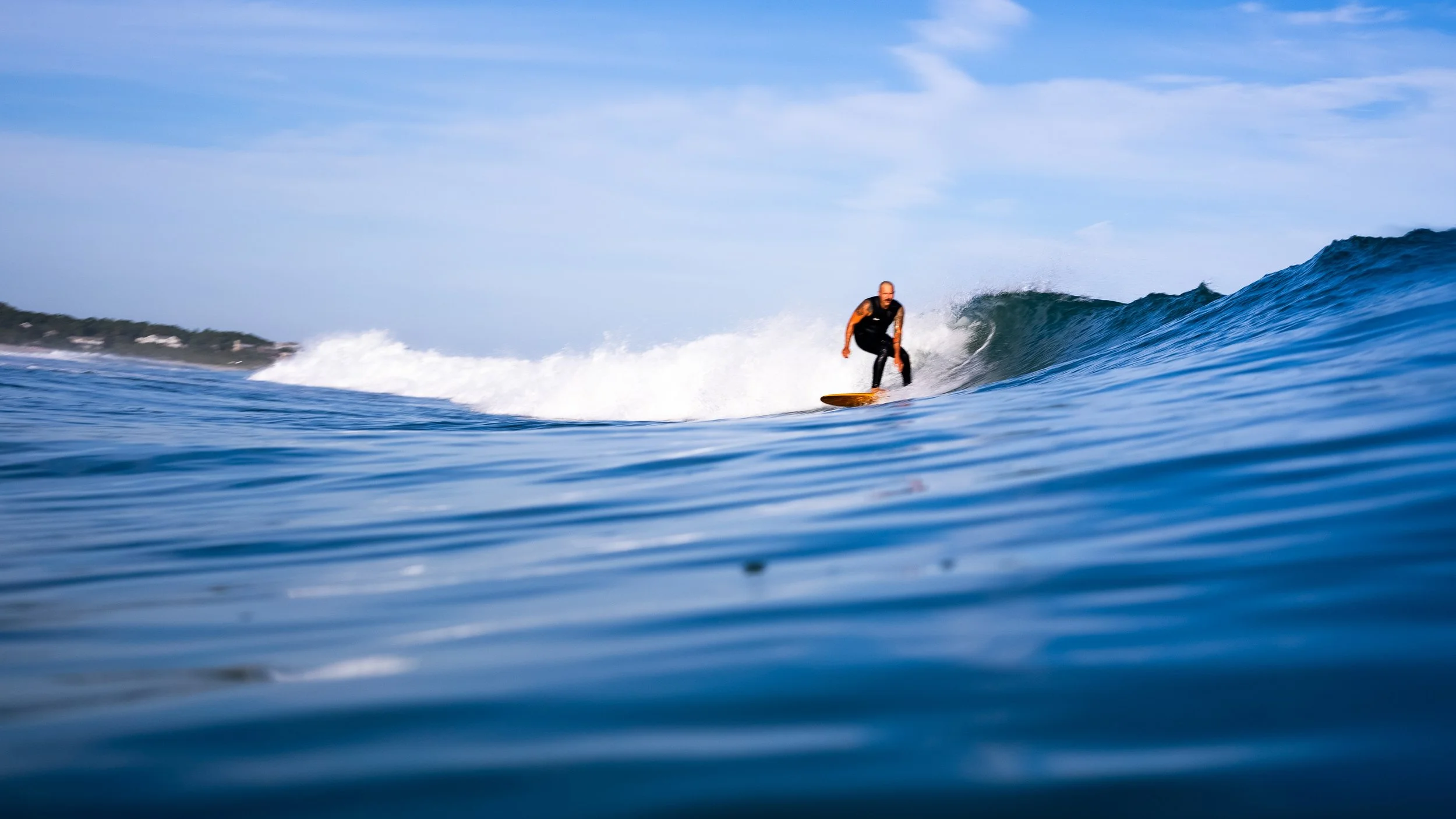 Surfer riding wave in ocean under blue sky.