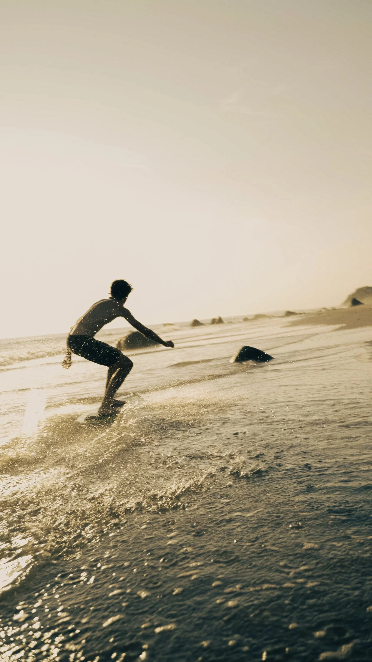 Person skimboarding on a sandy beach at sunset