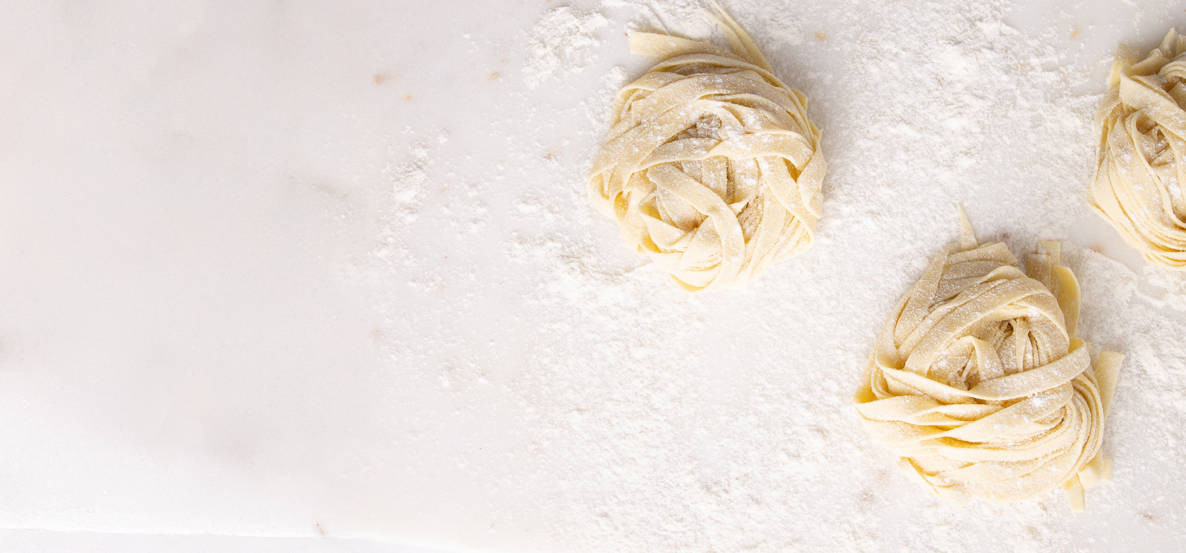Uncooked pasta nests sprinkled with flour on a white surface