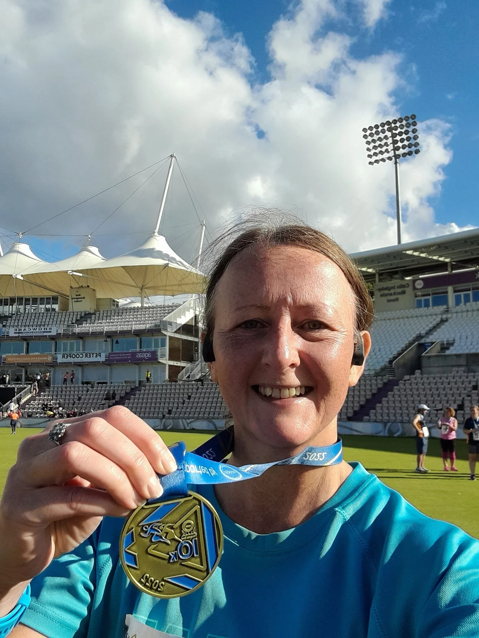 Person holding a medal on a sports field with a stadium in the background on a sunny day.