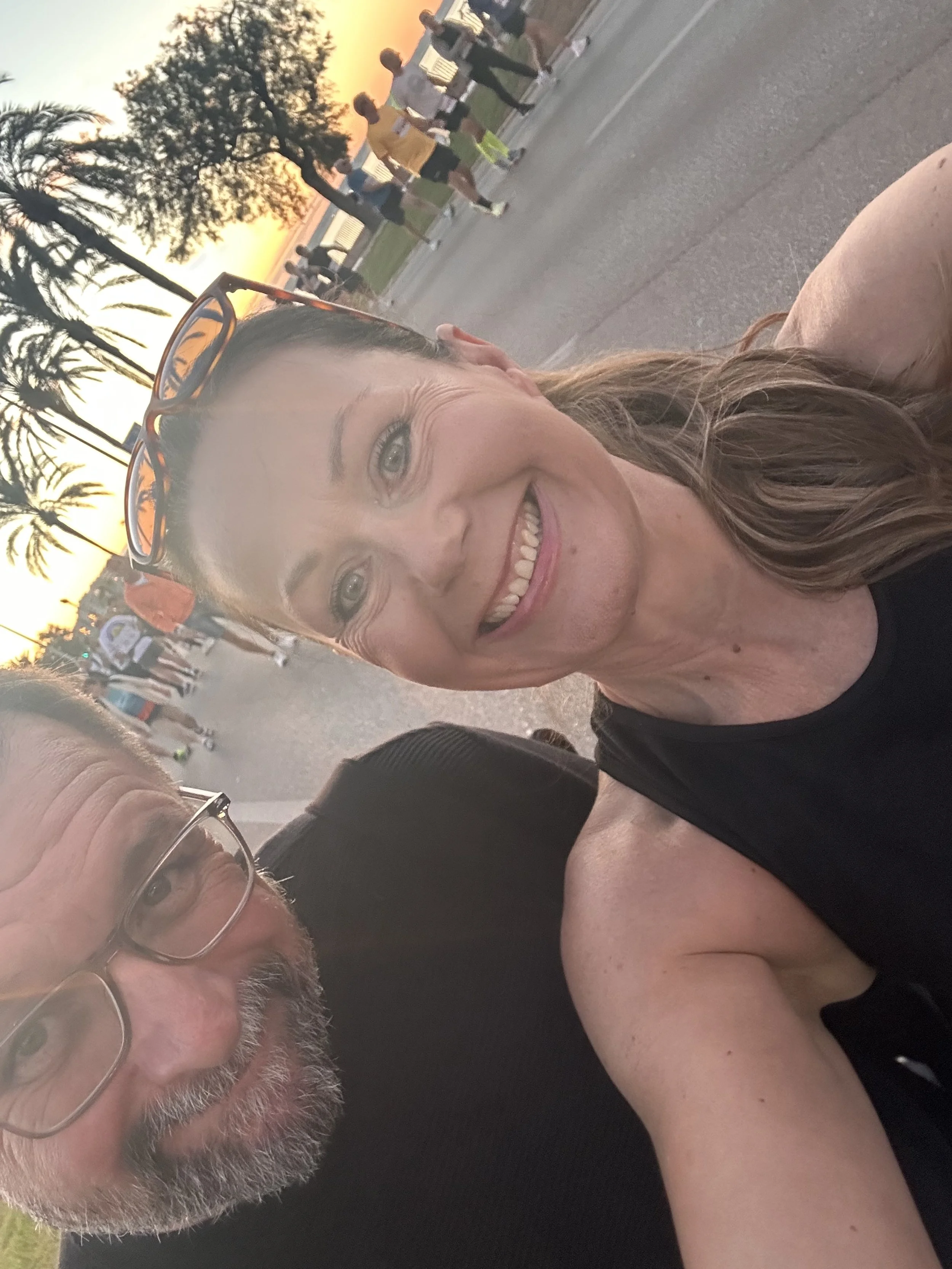 Two people taking a selfie with runners and sunset in the background.