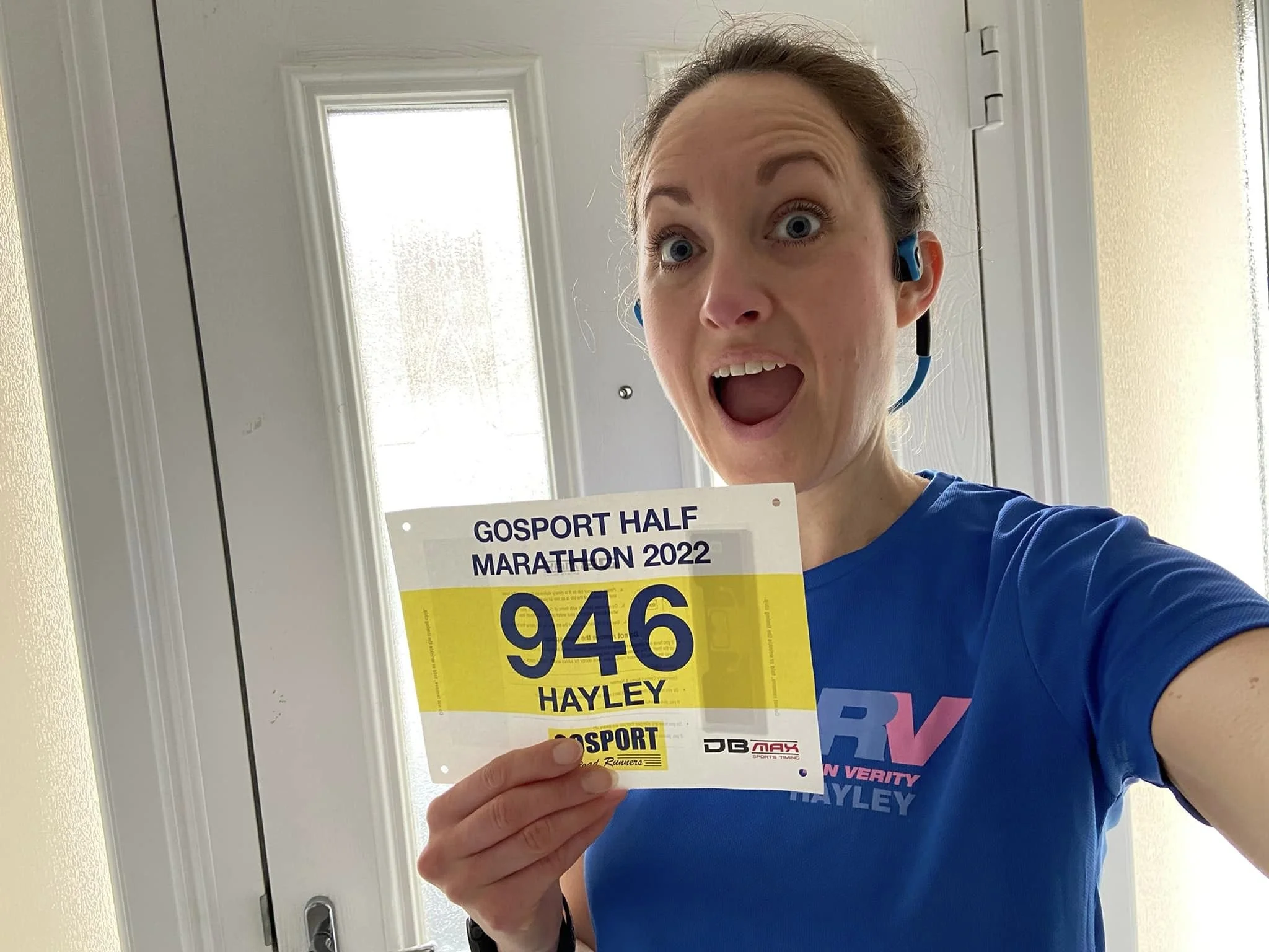 Person excitedly holding a Gosport Half Marathon 2022 race bib with the number 946, inside a room.