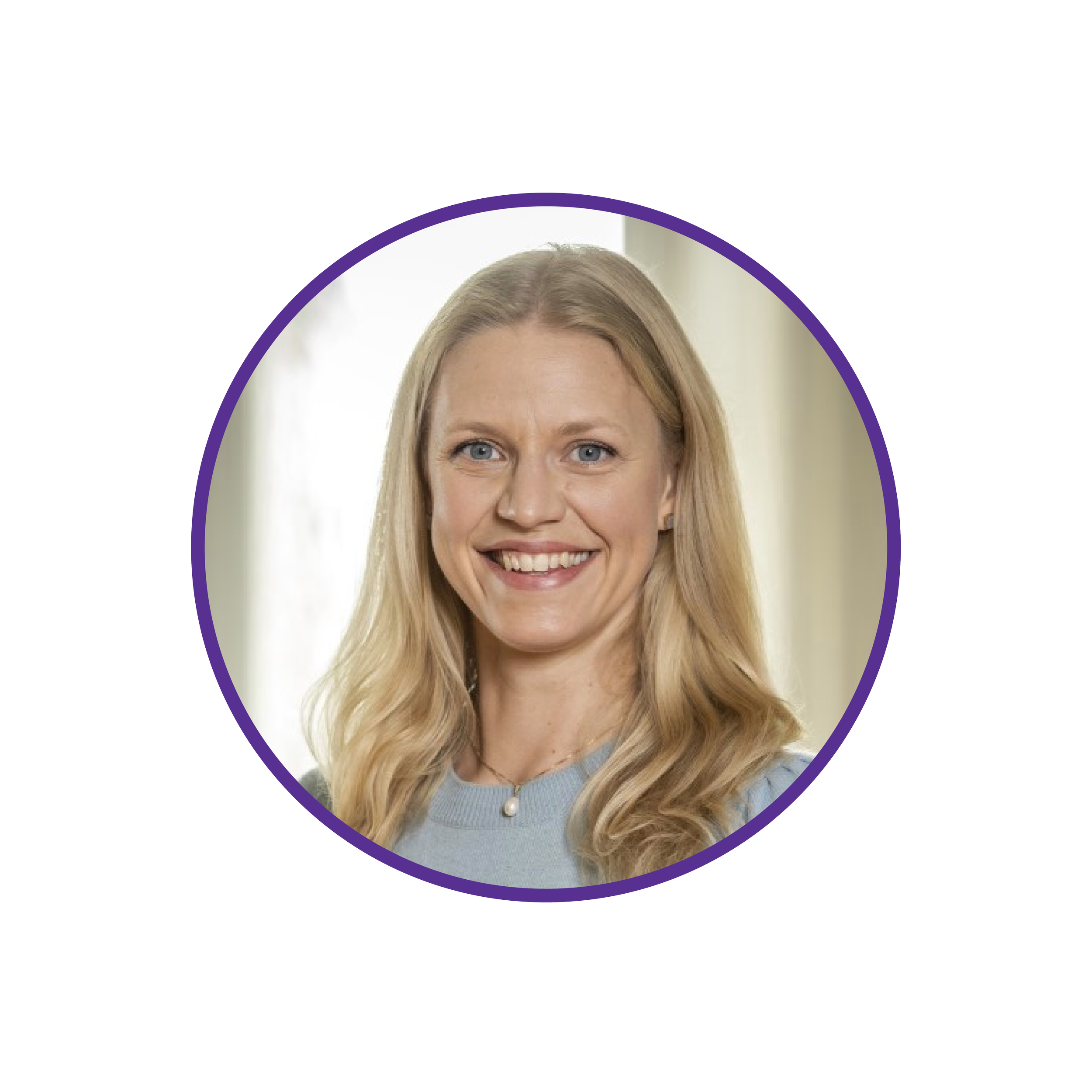 A headshot of a woman with long blonde hair wearing a light blue top and a pearl necklace, smiling in front of a blurred light-colored background.