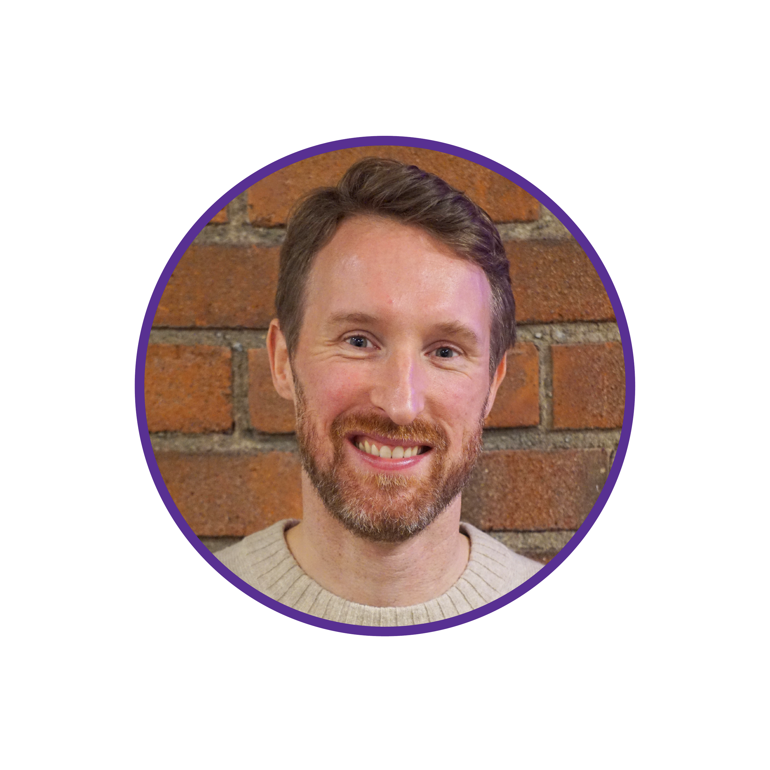 Headshot of a smiling man with short brown hair and a beard, standing in front of a brick wall.
