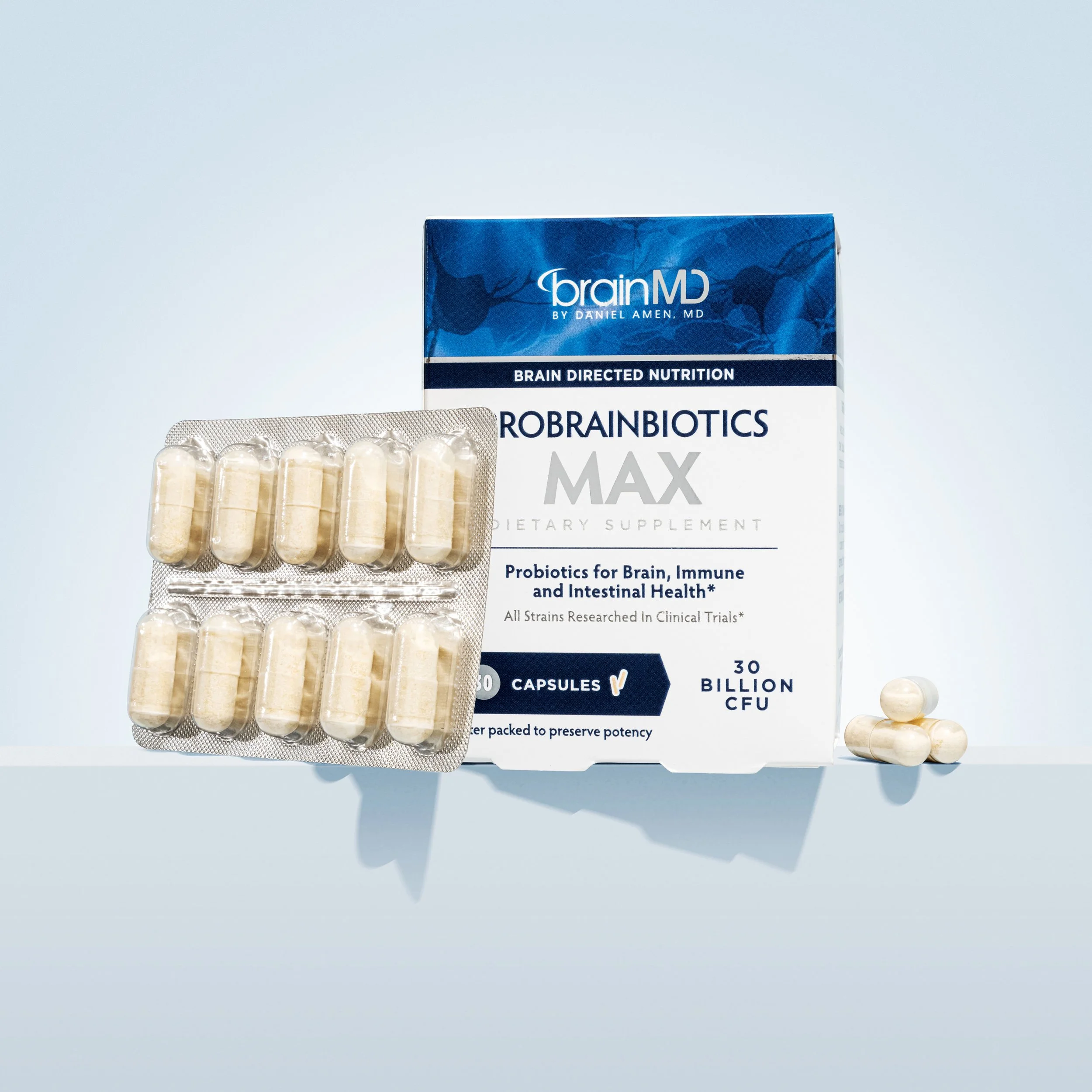 Box of BrainMD Probiotics MAX dietary supplement capsules with a blister pack of capsules placed in front and three capsules lying beside the box.