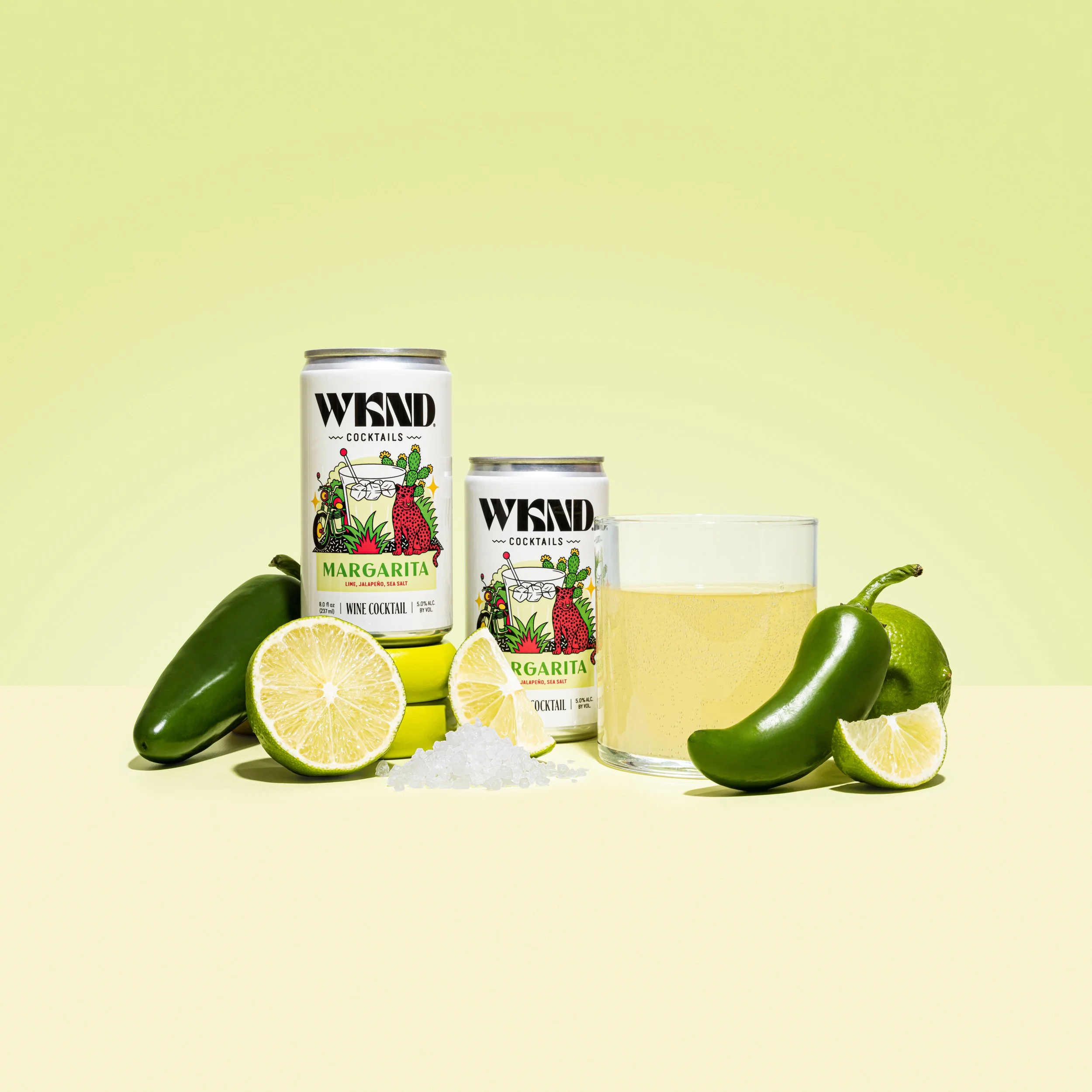 Canned margarita cocktail, fresh lime, jalapeño, sea salt, and a glass of margarita on a light background.