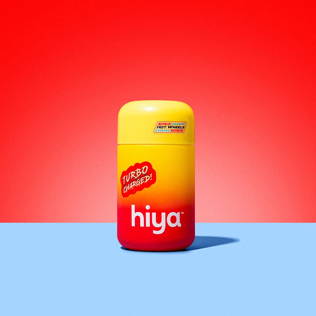 Container of Hiya lip balm with a yellow and red gradient design on a pastel background, featuring the words 'Turbo Charged!' and a label for 'Hot Wheels' on the lid.