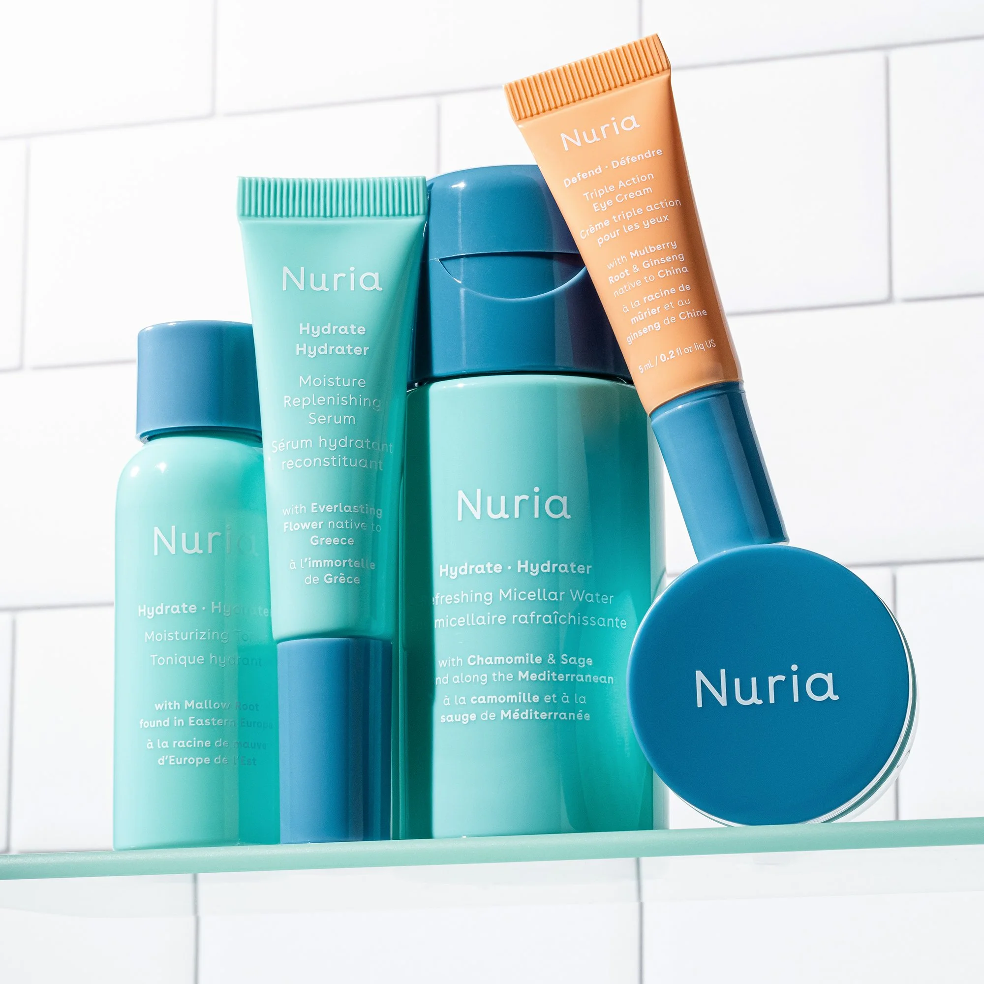 Collection of Nuria skincare products, including moisturizer, micellar water, and eye cream, arranged on a glass shelf in front of a white tiled wall.