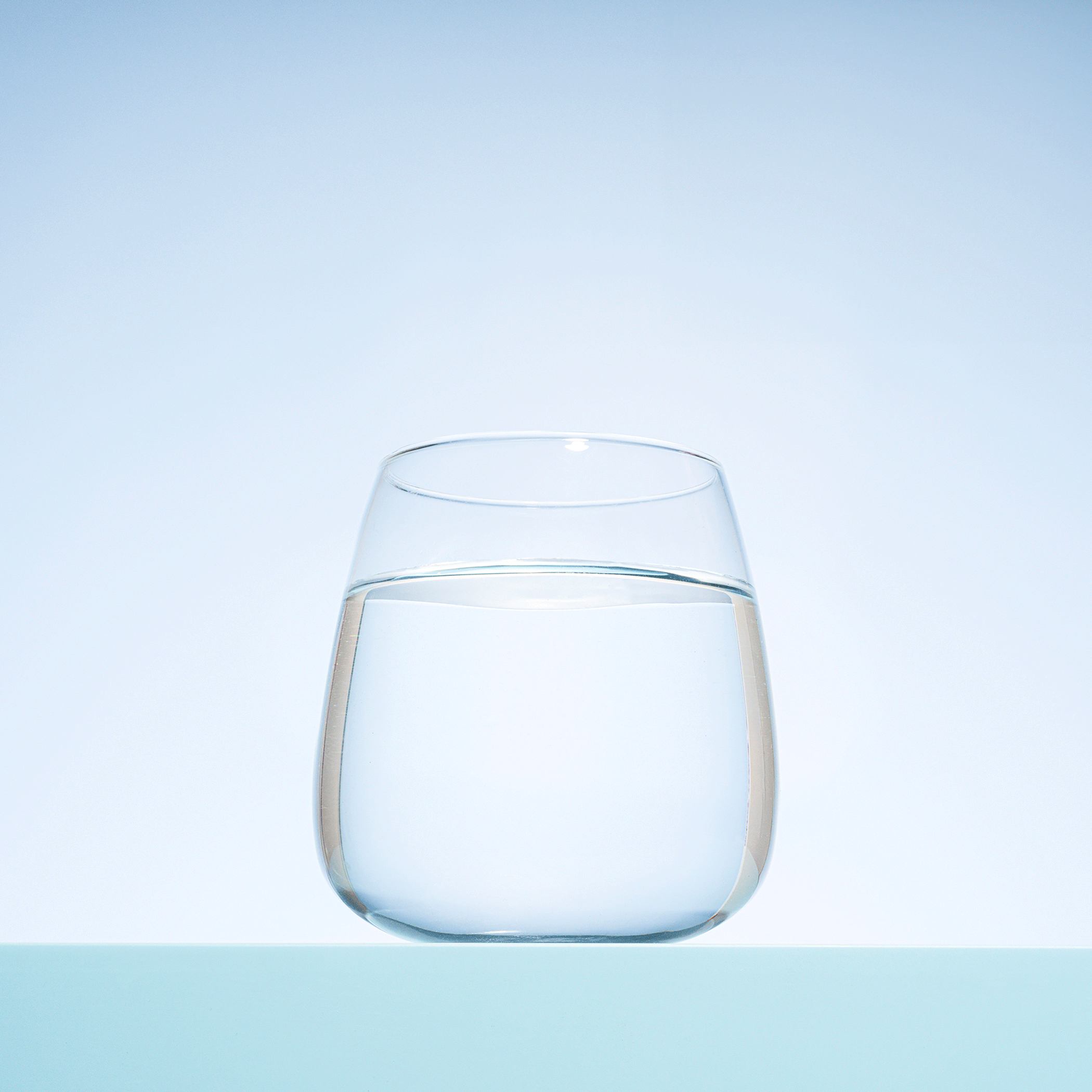 A clear glass of water on a light blue surface with a blue gradient background.