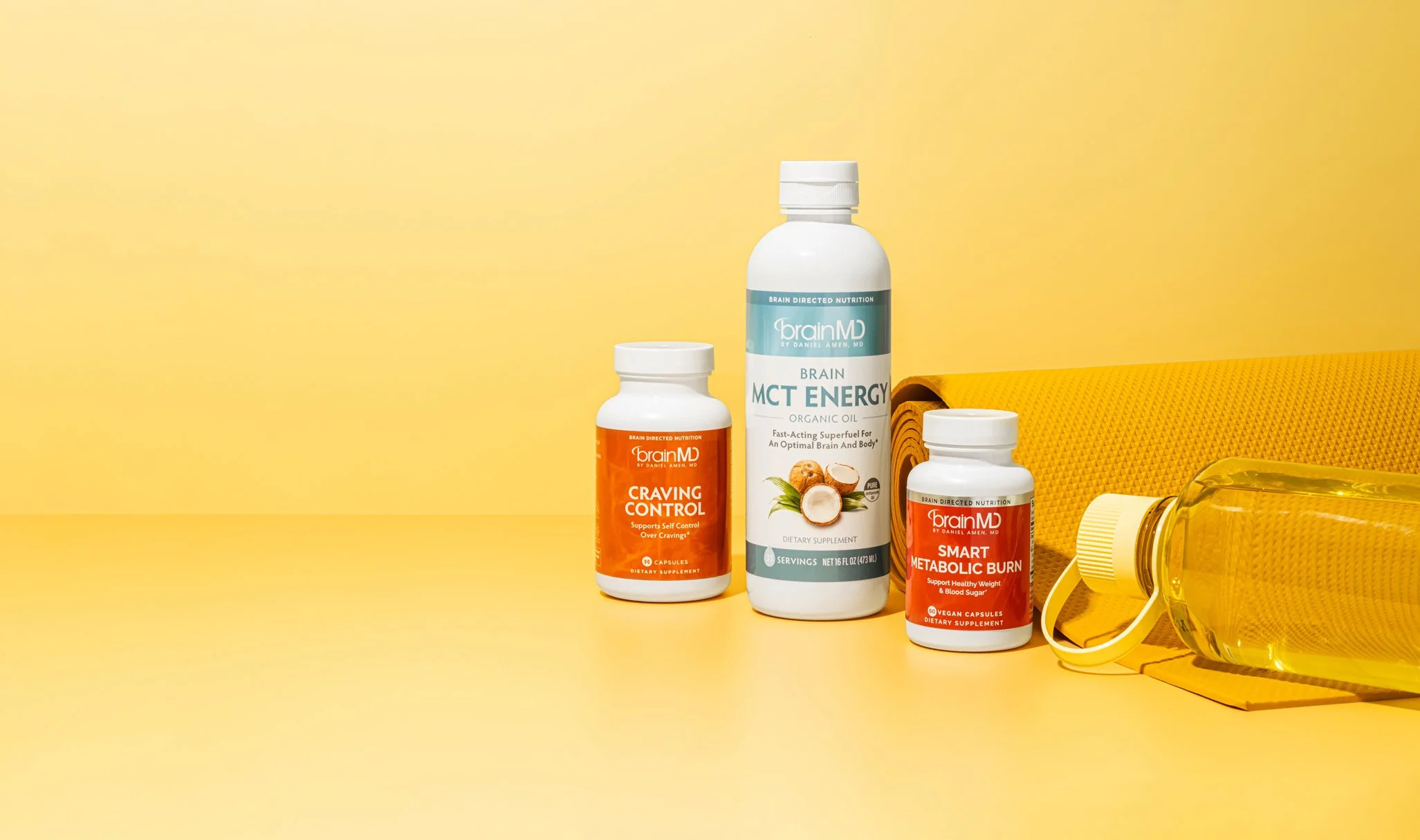 Supplements on yellow surface with rolled yoga mat, water bottle, and face mask