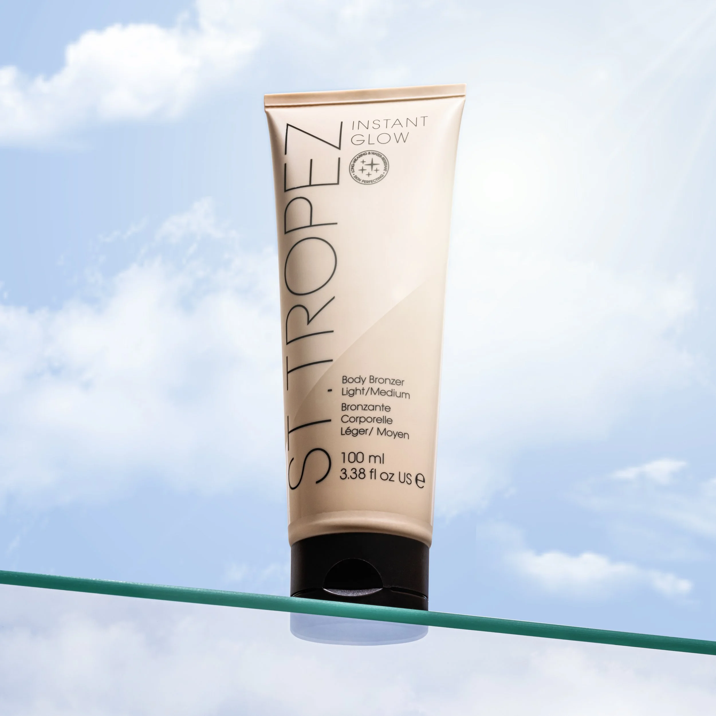 Tube of St. Tropez Instant Glow Body Bronzer in Light/Medium shade, resting on a clothesline with a cloudy blue sky background.