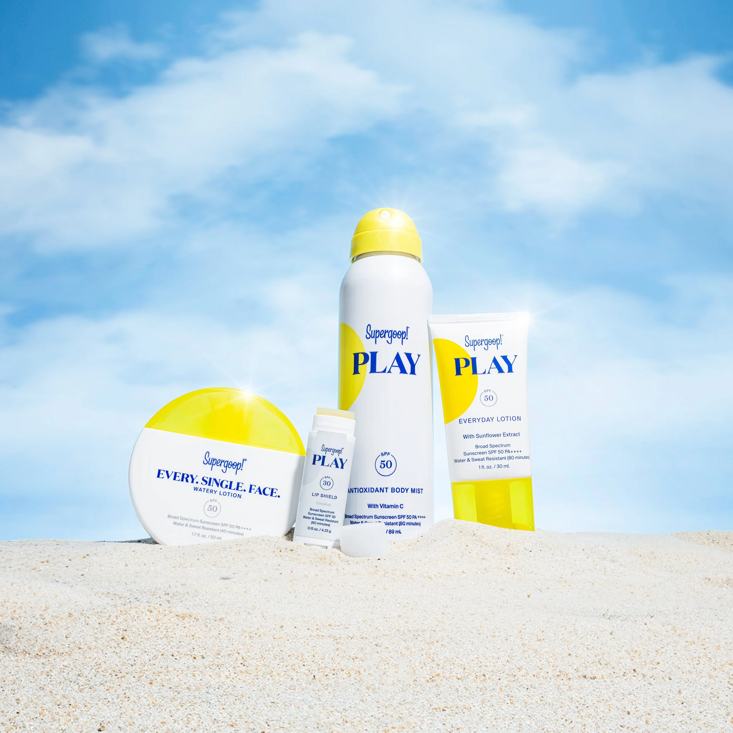 Various SPF sunscreen products on sandy beach with blue sky background