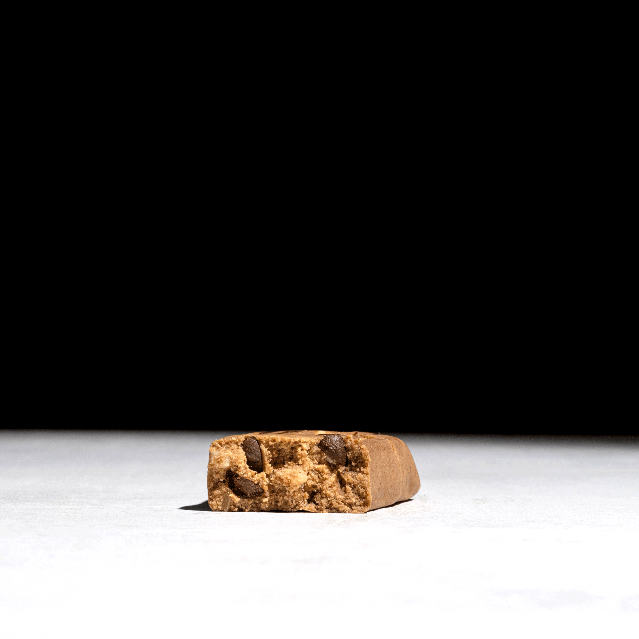 Close-up of a chocolate chip cookie bar on a white surface with a black background.