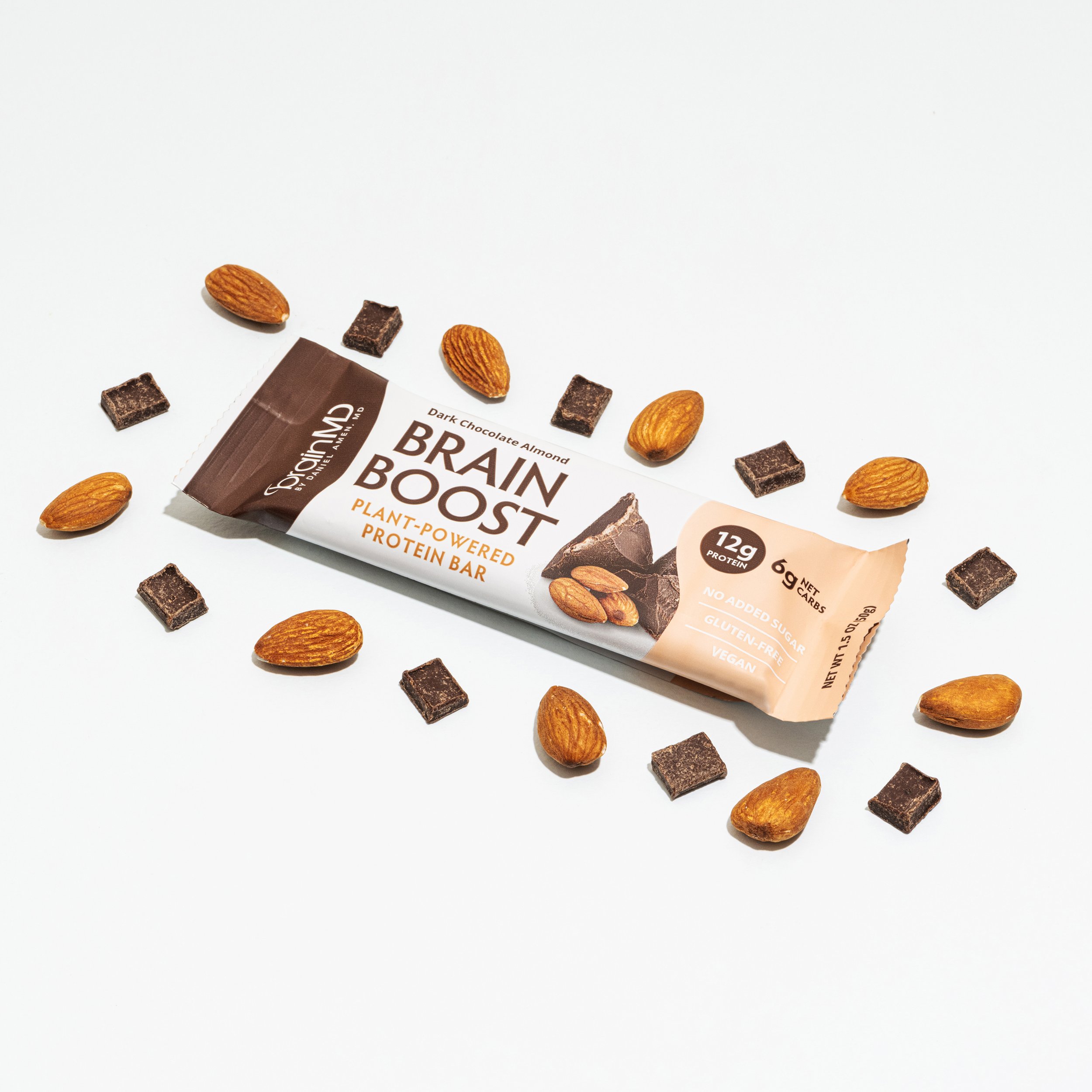 Plant-based chocolate almond protein bar called Brain Boost surrounded by almonds and chocolate pieces on a white background.